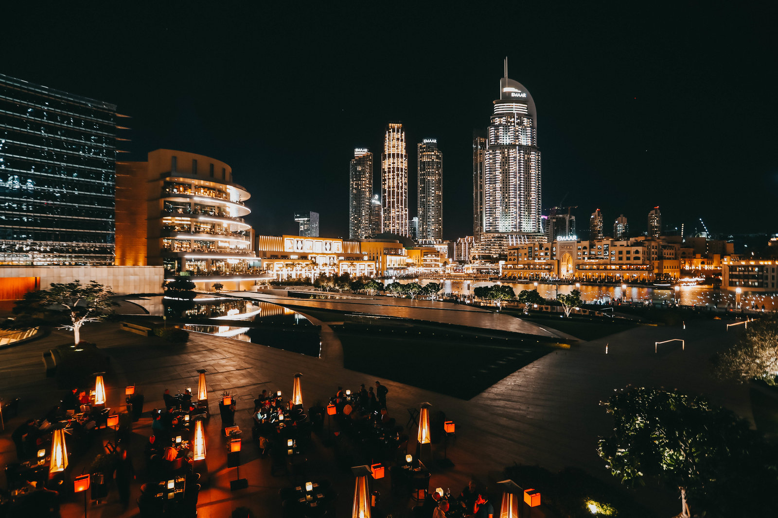 夜幕下，带有“EMAAR”标识的迪拜摩天建筑群灯火璀璨，滨水商圈流光溢彩。户外暖灯错落的休憩晚宴区域，参与活动的安利伙伴围坐交流，氛围轻松高端，尽显本次活动的高品质格调。