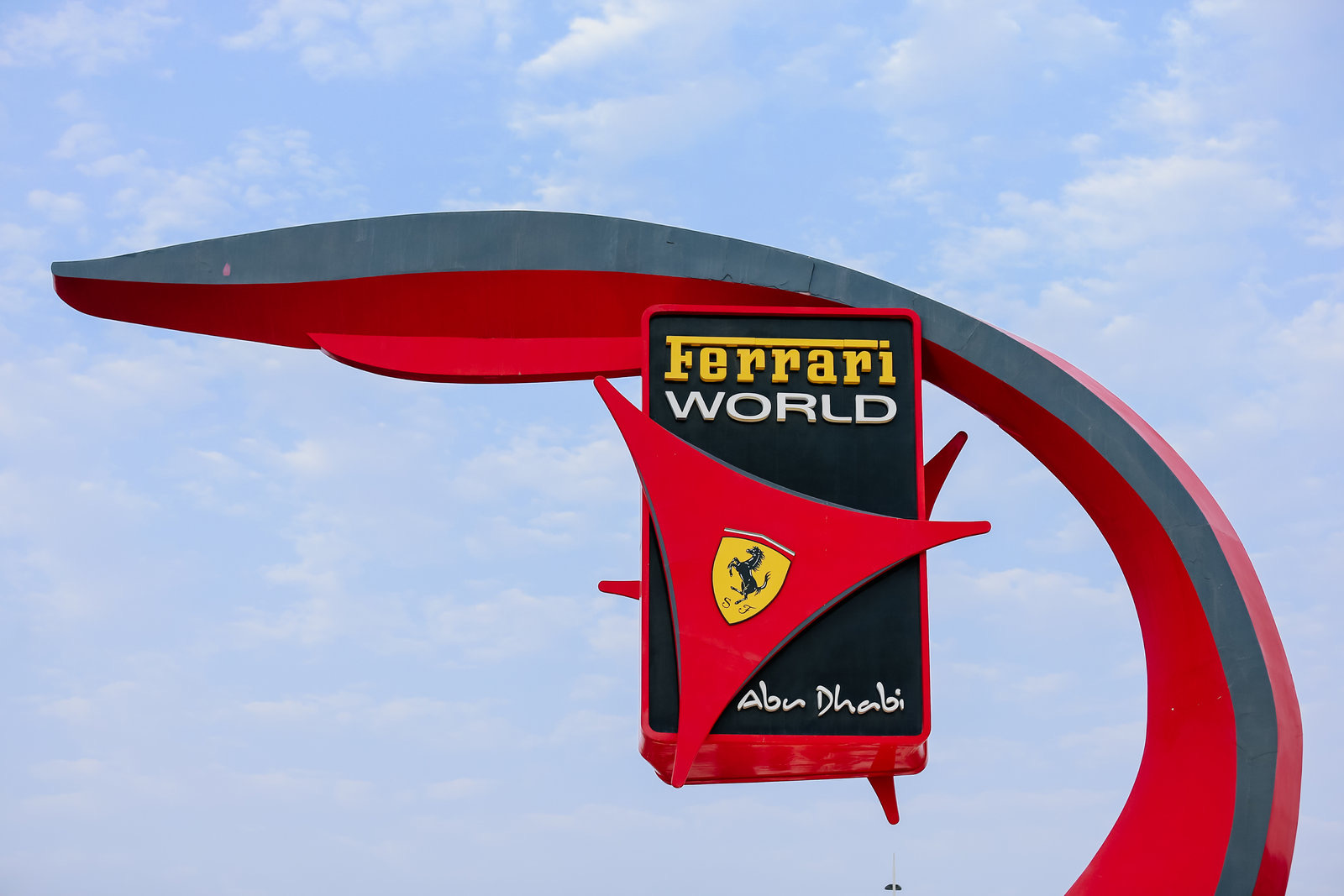澄澈蓝天之下，带有“Ferrari WORLD”“Abu Dhabi”字样及法拉利跃马品牌标识的园区标牌醒目亮眼，红灰流线设计动感十足。此处是安利海外研讨行程的打卡站点，整体氛围明快活力，尽显旅程的丰富趣味与高端质感。