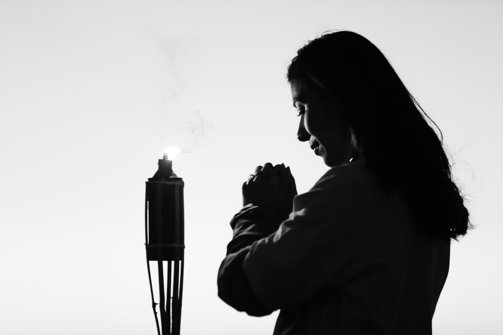 画面为黑白剪影风格，安利活动现场，长发伙伴双手合十，面向正在燃烧的火种虔诚祈愿，整体氛围沉静温暖，满含伙伴对事业发展、品牌前行的美好期许，传递出诚挚的信念感与向新而行的力量。