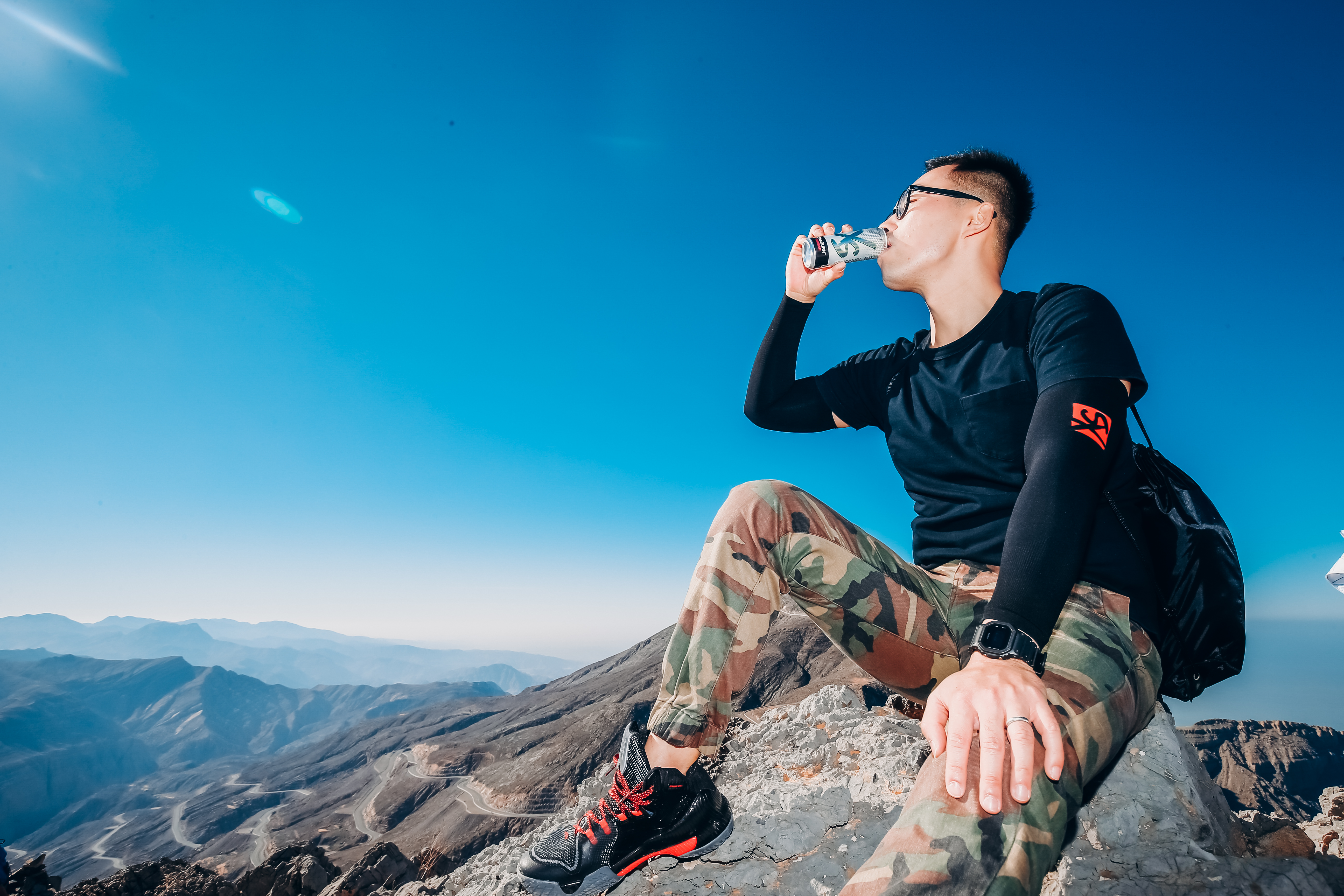 澄澈碧空之下，身着运动装束的男士登顶山巅，背靠连绵壮阔的层叠山脉，正饮用安利XS饮料补充能量。画面开阔明快，满溢蓬勃向上的活力，彰显安利倡导的健康活力生活方式，凸显XS饮料适配户外运动场景的属性。