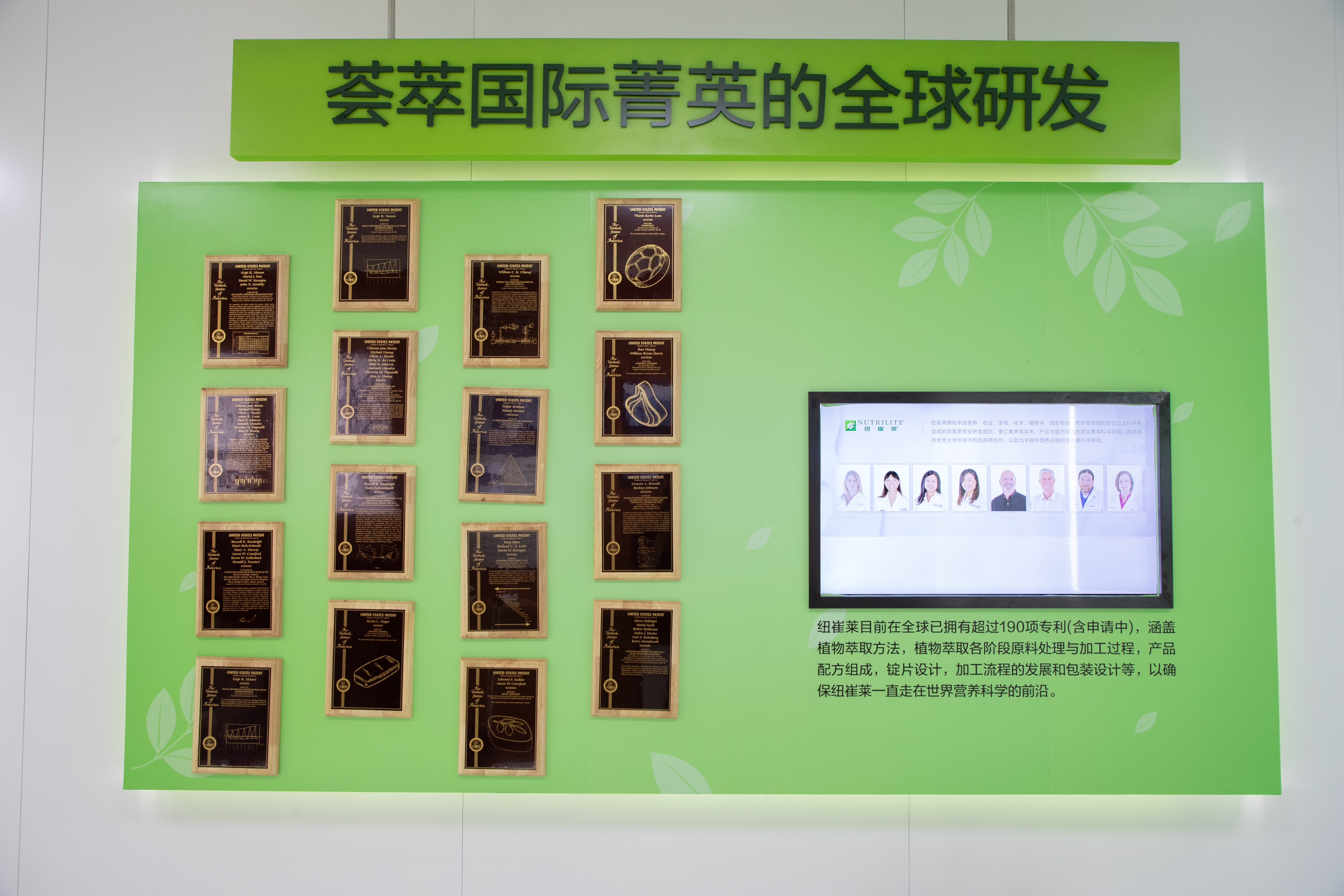 这面展示墙主题为“荟萃国际菁英的全球研发”，墙面陈列多块专利认证奖牌，右侧屏幕展示纽崔莱研发团队信息，标注纽崔莱全球已拥有超190项专利（含申请中），覆盖研发生产全流程相关领域，尽显品牌雄厚研发实力与行业领先地位。