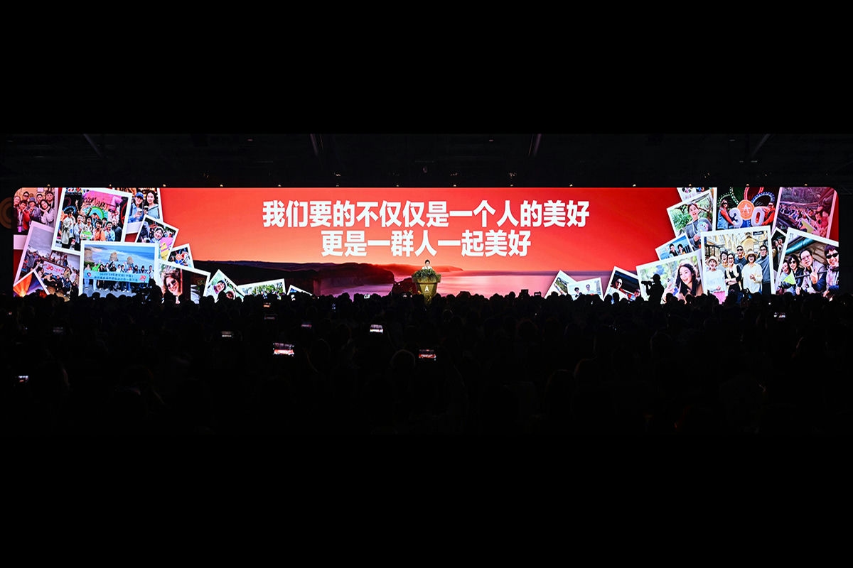 活动现场巨幅主屏幕展示核心标语“我们要的不仅仅是一个人的美好，更是一群人一起美好”，屏幕两侧排布着众多安利伙伴的活动留影，台上人员正在宣讲，台下坐满参会伙伴，不少人举手机记录现场内容，氛围热烈积极，彰显安利共筑美好的品牌理念。