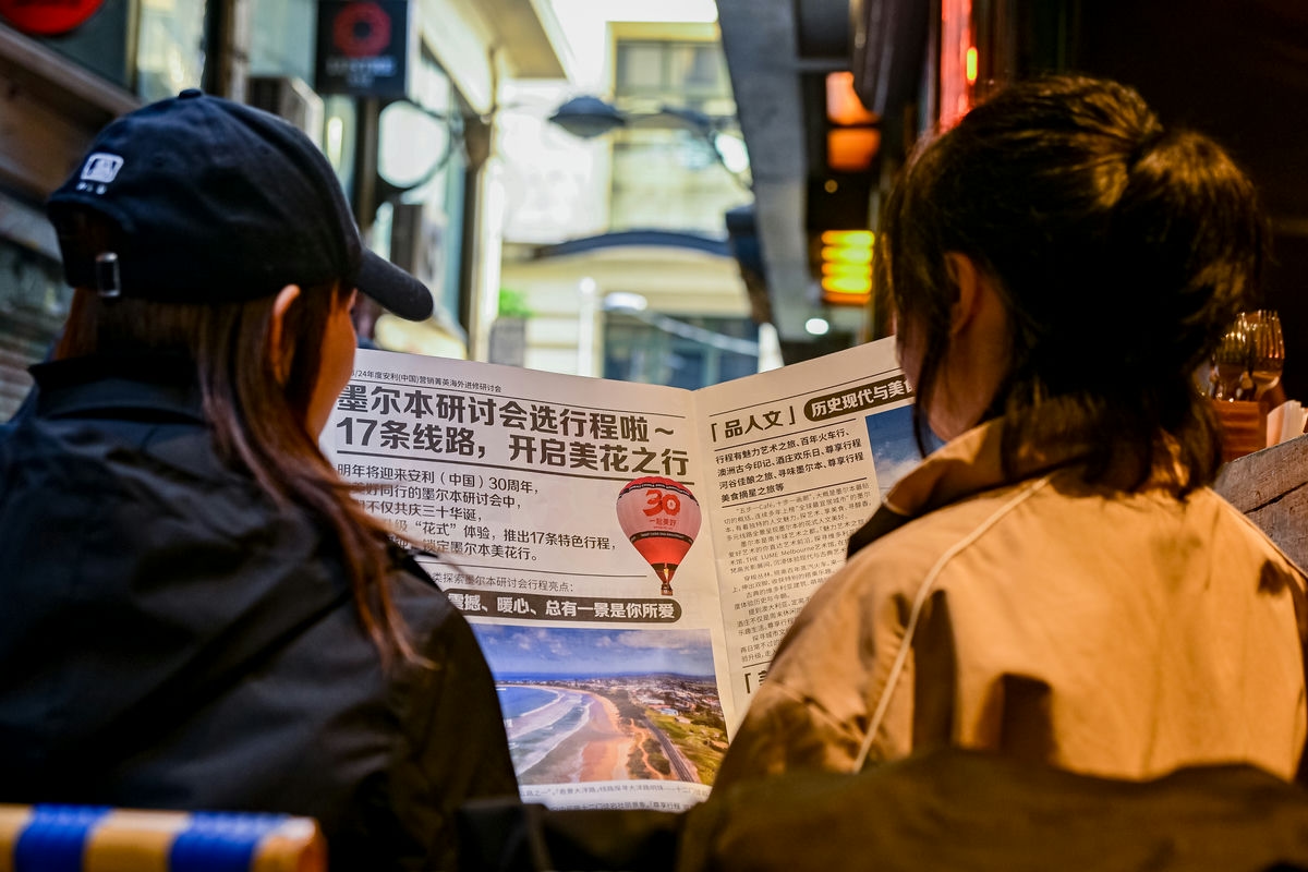 画面中两位安利营销伙伴正一同查阅24年度安利（中国）营销菁英海外进修研讨会相关宣传物料，本次研讨会落地墨尔本，恰逢安利中国30周年，将推出17条特色线路开启美花之行，氛围轻松热切，尽显伙伴对此次行程的期待。