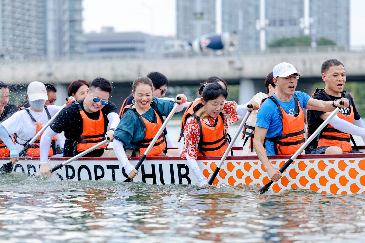 画面中参与团建的安利伙伴们身着橙色救生衣，乘坐印有“SPORT HUB”字样的龙舟，共同持桨奋力划行，水面水花飞溅，众人神情饱满斗志昂扬，氛围热烈向上，充分展现出安利团队凝心聚力、协作共进的精神风貌。